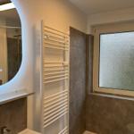 Badezimmer mit Dusche, Heizkörper und gefliestem Fensterbereich.
