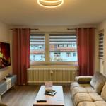 Wohnzimmer mit Sofa, Fernseher und Fenster mit Blick auf Gebäude