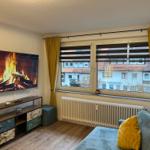 Wohnzimmer mit TV, Sofa und Fensterblick auf Gebäude.