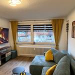 Wohnzimmer mit Sofa, Fernseher und Fenster mit Blick auf Gebäude.