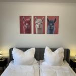 Zwei Betten mit weißen Kissen und Decken. An der Wand hängen drei Bilder von Alpakas.