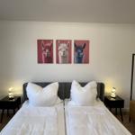 Zwei Betten mit weißen Bettwäschen, Wandbild mit drei Alpakas und Nachttische mit Lampen.