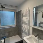 Badezimmer mit Dusche, Waschbecken und beleuchtetem Spiegel.