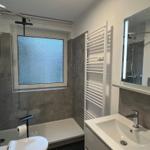 Badezimmer mit Dusche, Waschbecken und Toilette. Fenster mit getöntem Glas.