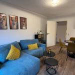 Blauer Sofa mit gelben Kissen, Essbereich mit Tisch und Stühlen, Wandbilder mit Lamas.