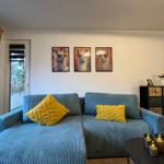 Ein Wohnzimmer mit blauem Sofa, gelben Kissen und drei Wandbildern von Lamas.