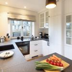 Küche mit weißen Schränken, dunklem Arbeitsplatz und Fensterblick auf die Straße.