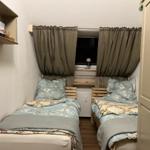 Two single beds with blue bedding are under a window with curtains.