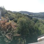 View from balcony over green hills and settlement under trees.