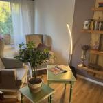 Room with two armchairs, plant, table, and bookshelf on the wall.