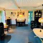 Living and dining area with table, chairs, sofa and fireplace. Wooden walls and blue carpet.