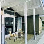 Deck with table and two chairs under white roof. Wooden planks and green walls.