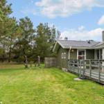 Green wooden house with terrace and garden among trees.