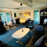 Living room with leather sofa, dining table, and ceiling fan. Light wall paneling and large windows.