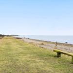 A grassy path runs alongside a pebbled beach to the sea. A wooden bench is in the foreground.