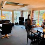 Living and dining area with wooden ceiling, TV, wood stove, and large windows.