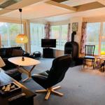 Living room with seating, TV, and wood stove. Large windows offer ample daylight.