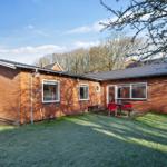 A red brick house with a garden and terrace with red chairs.