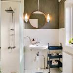 Bathroom with shower, sink, and toilet. Round mirror and blue rug.