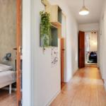 Hallway with wooden floor and bedroom. Wall shelf with plant. Doors to other rooms.