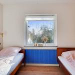 Two beds with pink bedding stand by a window with a blue radiator below.