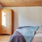 Bedroom with bed, wooden wardrobe, and wooden ceiling. Window and wall lamp visible.