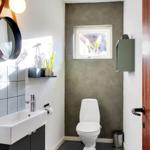Bathroom with toilet, sink, and window. Gray wall, dark tiles.