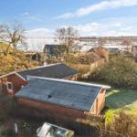 Red brick house with gray roof, surrounded by green areas and trees, view of a harbor.