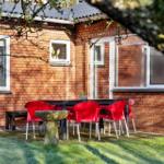 Red seating area with table and stone basin in garden in front of brick house.