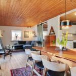 Dining area with wooden table and chairs, kitchen and living room with sofa and wooden ceiling.