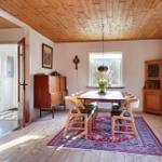 Dining room with wooden ceiling, table, chairs, and rug. Corridor to the kitchen.