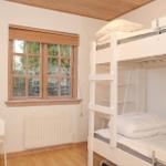 Room with bunk bed, desk, and window with wooden frame.