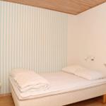 Bedroom with bed, striped wall, and wooden ceiling. Window with blinds.