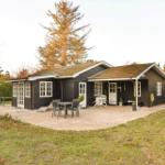 Black wooden house with patio, garden, and seating areas.