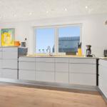 Modern kitchen with white cabinets, wooden floor, and window with view of roof.