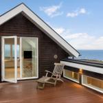 Deck with wooden lounger and ocean view. Glass doors lead inside.