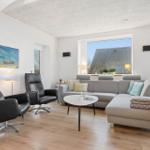 Living room with gray sofa, two black chairs, and wooden floor. Large windows and wall art.