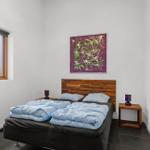 Bedroom with bed, nightstands, and wall art. Window shows exterior view.