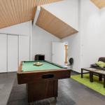 Room with pool table, sofa, and green rug. Wooden ceiling and white walls.