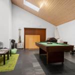 Room with pool table, sofa, table, and green rug. Wooden ceiling and black tiles.