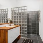 Bathroom with sink, shower, and mirror. Glass blocks and dark tiles.