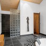 Shower with glass block wall, hot tub, and sauna in room with wooden ceiling and large window.