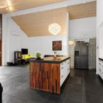 Kitchen with island, black countertop, and white cabinets. Wooden ceiling and large window.
