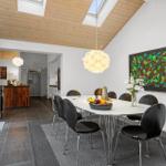 Dining area with table, chairs, and wall art. Kitchen in background. Wooden ceiling with skylights.