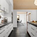 Kitchen with white cabinets, black countertops, and wooden ceiling. View into dining area with table and chairs.