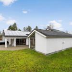 Modern villa with solar panels, terrace, and garden. Surrounded by trees and grass.