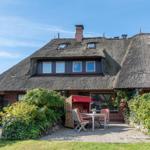 Haus mit Strohdach, Garten mit Tisch, Stühlen und Rattanliege.