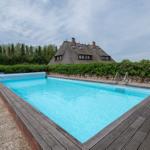 Pool mit Holzrand und Blick auf ein Haus mit Strohdach.