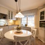 Küche mit Essbereich, weißer Tisch, Stühle und Fenster mit Jalousie.