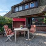 Terrasse mit Tisch, zwei Stühlen und einem Liegestuhl unter rotem Sonnenschutz.